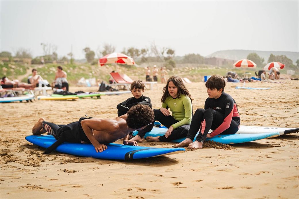 Private surf instructor demonstrating pop-up technique on the beach in Taghazout