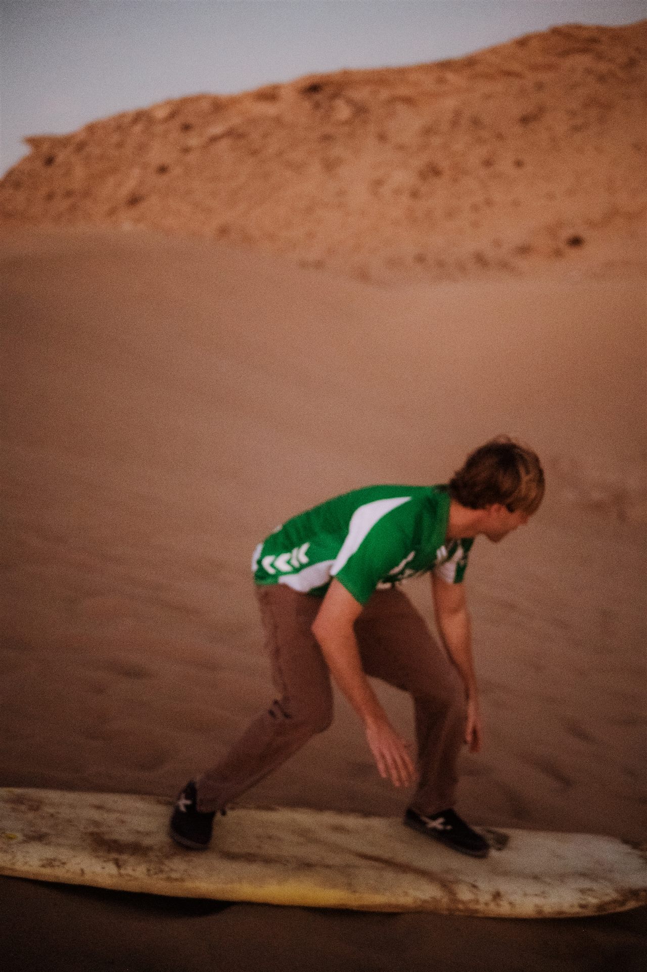 Tourist sandboarding solo down a steep dune near Taghazout, Morocco
