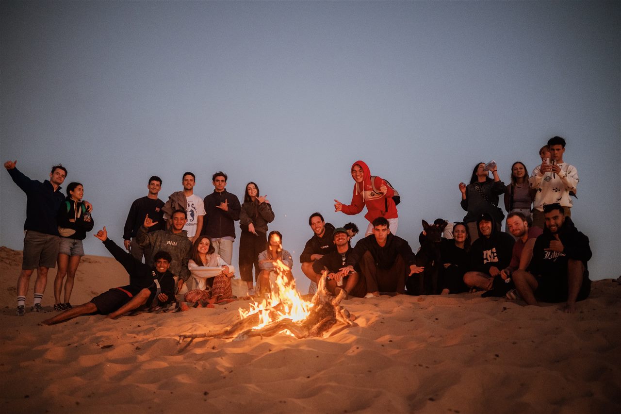 Large group of tourists around a bonfire at sunset after sandboarding near Taghazout